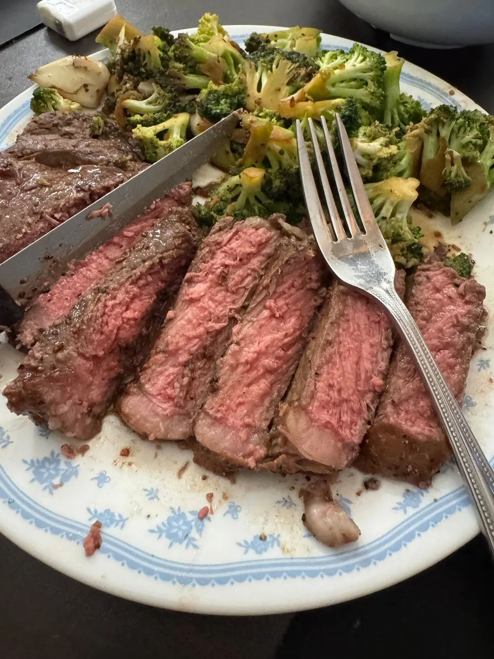 Slices of pink-centered steak beside seasoned broccoli and potato pieces.