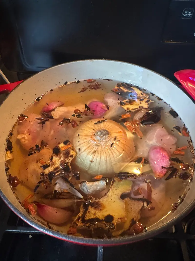 Onions, shallots, mushrooms, and charred aromatics steeping in liquid in a Dutch oven.