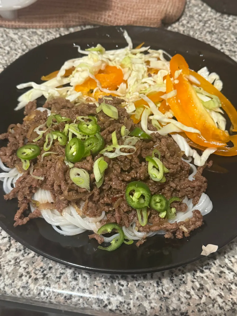 Rice noodles topped with browned ground meat, green chilis, scallions, cabbage, and orange pepper strips.