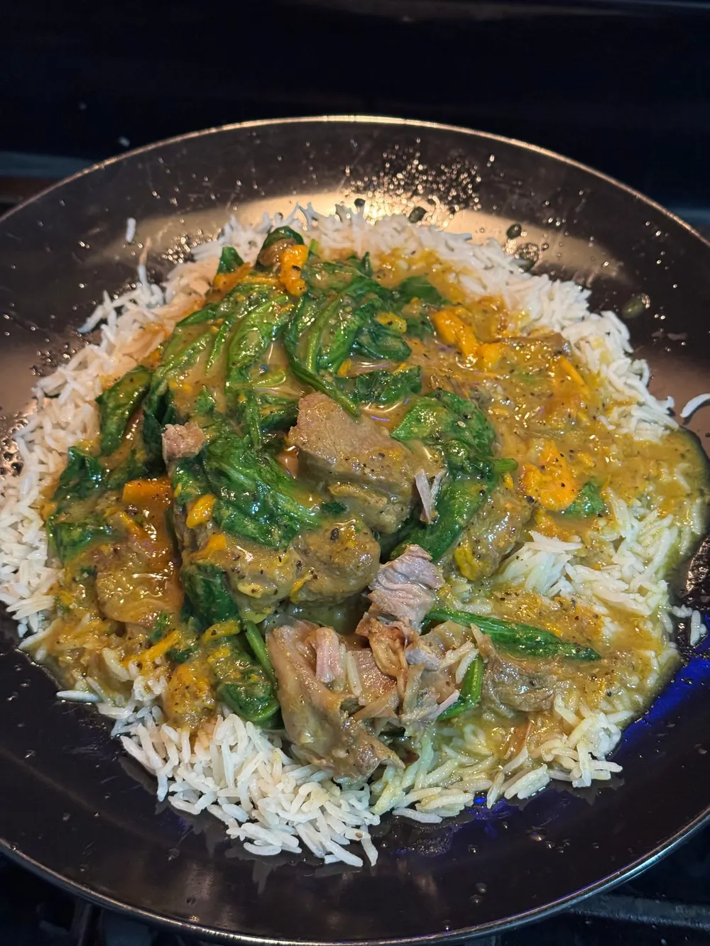 White rice topped with pieces of meat, spinach, orange vegetables, and a thick golden-brown sauce.