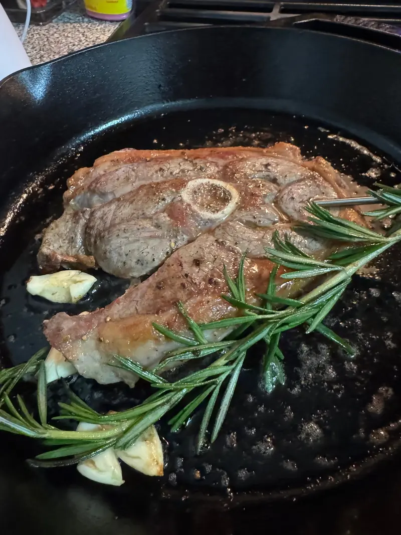 Thin steaks searing in a cast-iron skillet with rosemary, garlic, and onion rings.
