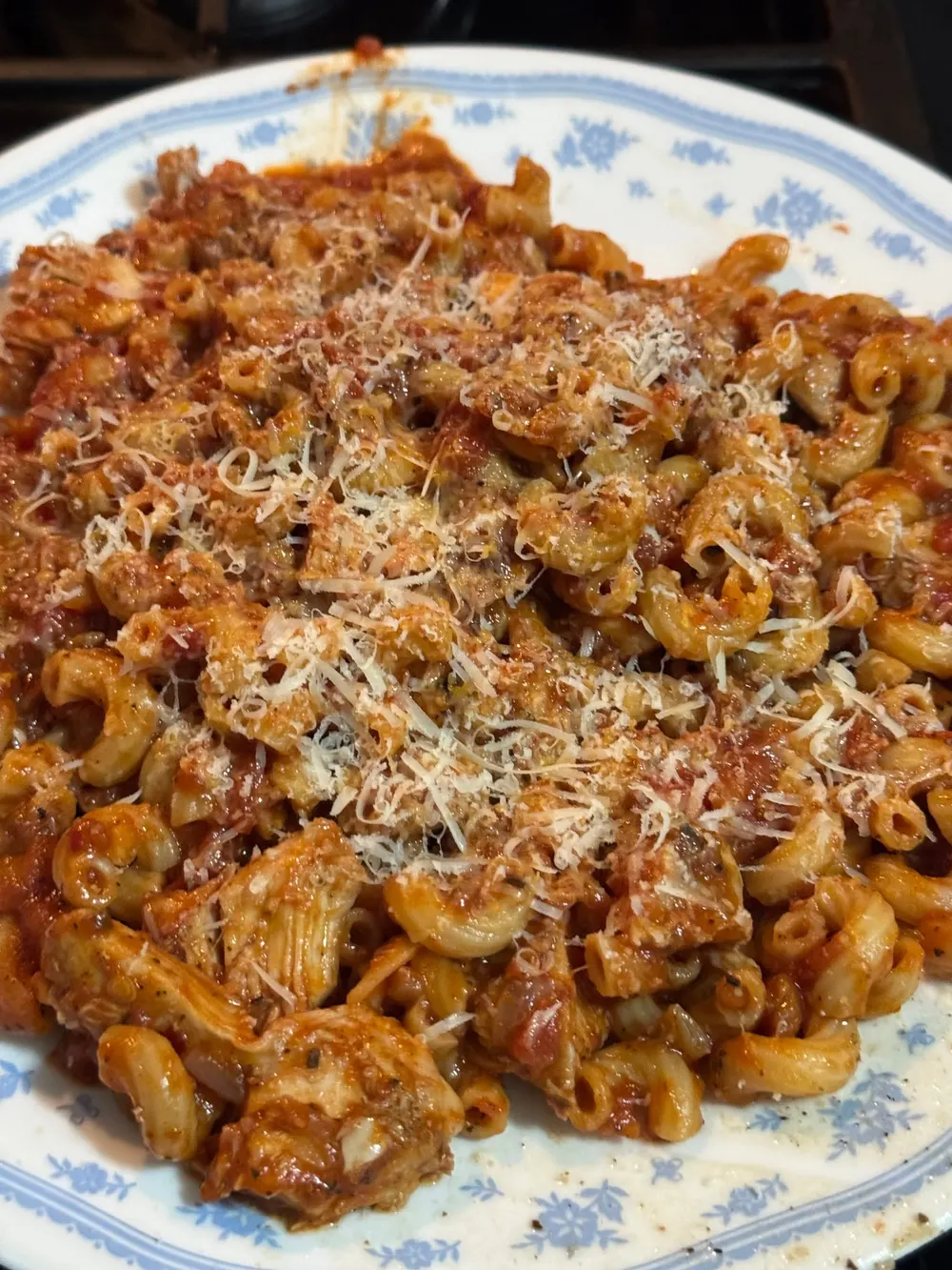 Elbow pasta in red sauce with pieces of meat and a layer of finely grated cheese on a patterned plate.